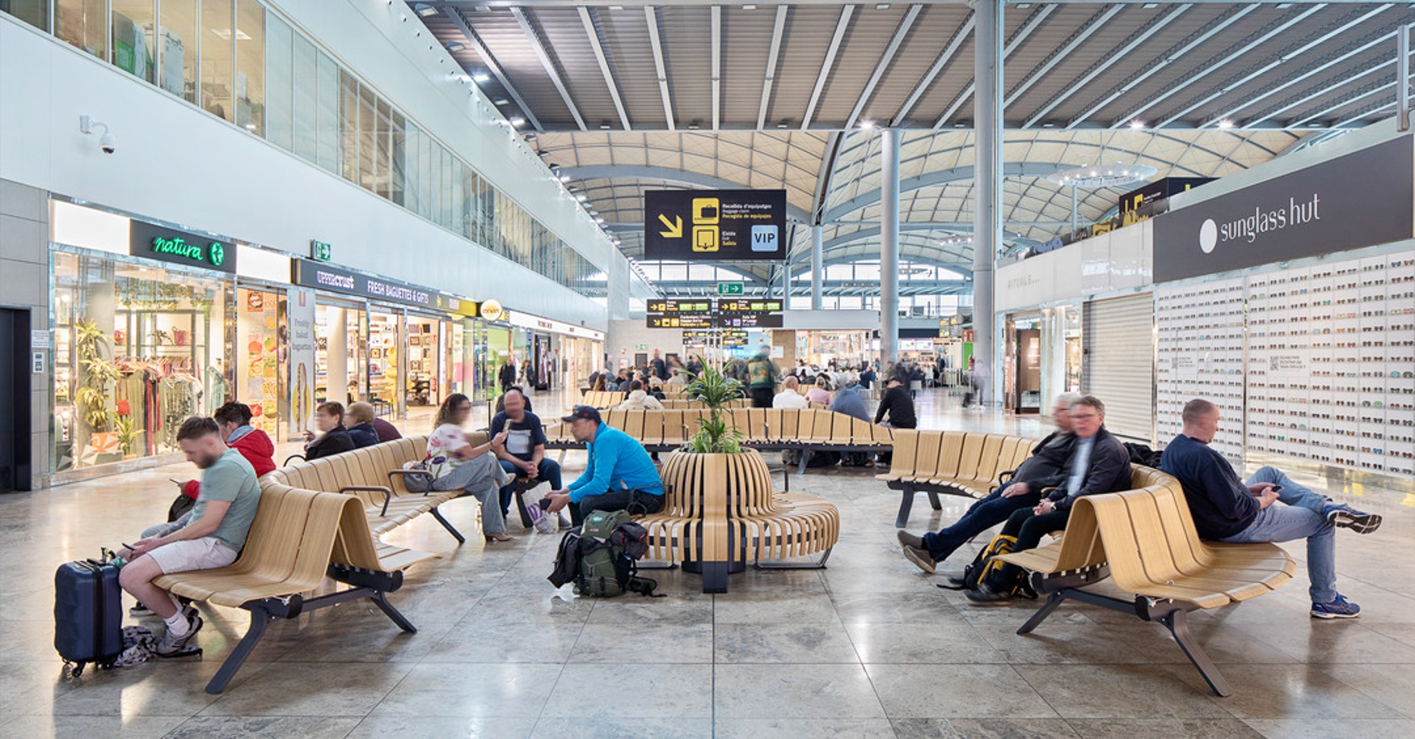 Travelers waiting among shops and seating in a busy airport concourse