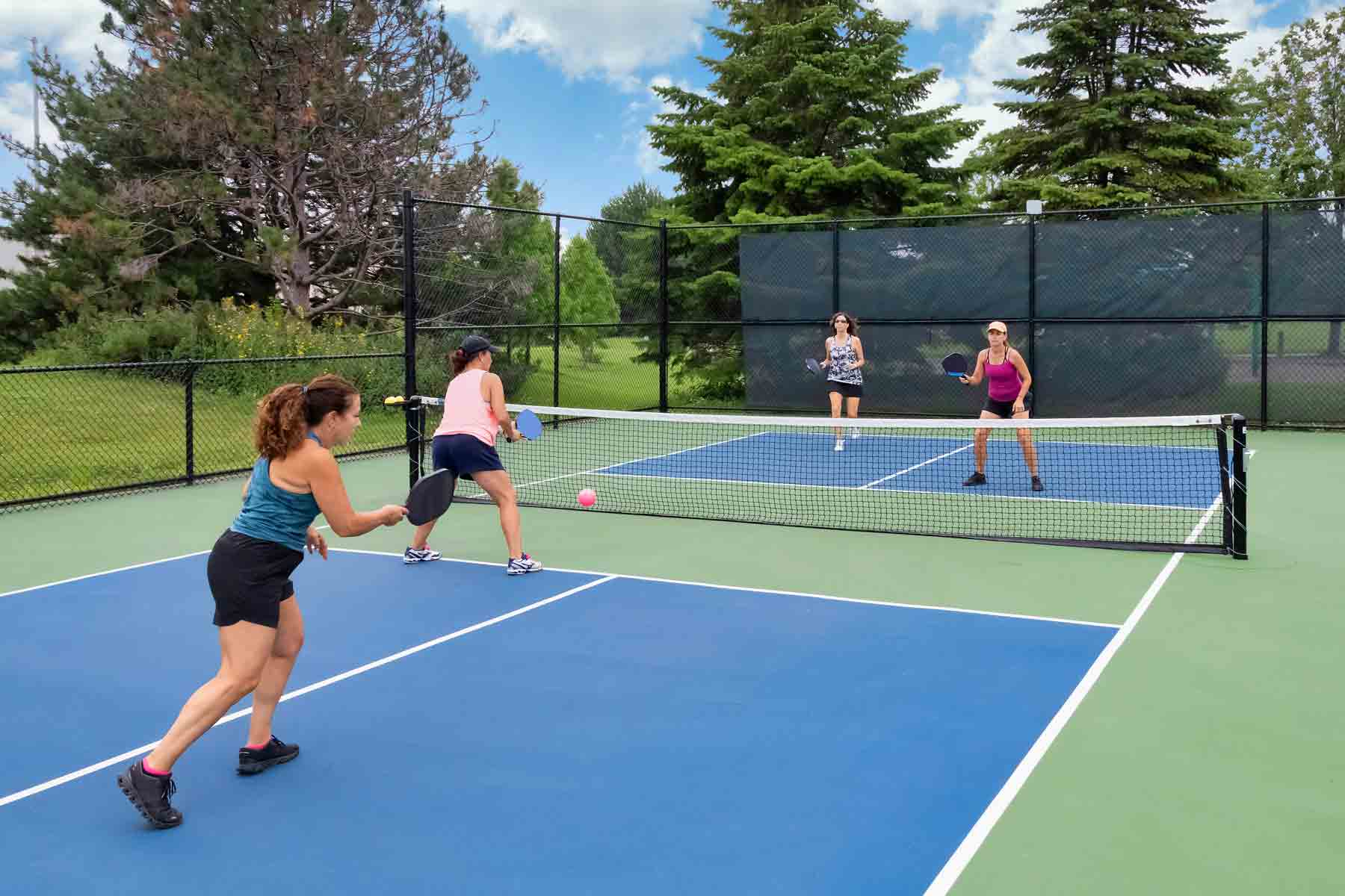 Four women playing pickleball together on an outdoor neighborhood court